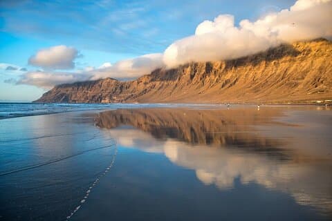 Beach beneath the Famara cliff
The trickle of water that remains on its flat, golden sand shore reflects the majesty of its 410 meters of height.