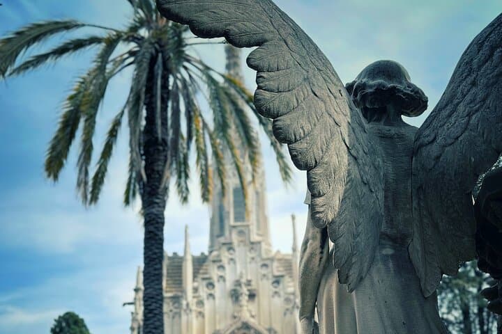 A view of one of the art nouveau mausoleums with an angel sculpture in the foreground on the montjuic cemetery tour