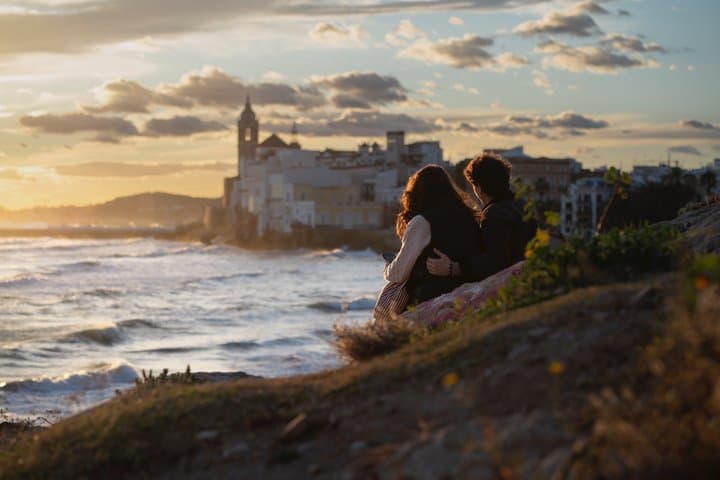 Couple overlooking Sitges during golden hour with the Church Sant Bartolomeo and Santa Tecla in the background.
