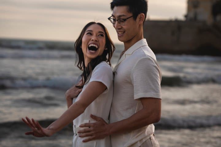 Newly engaged couple celebrating with laughter on a Sitges beach at sunset.