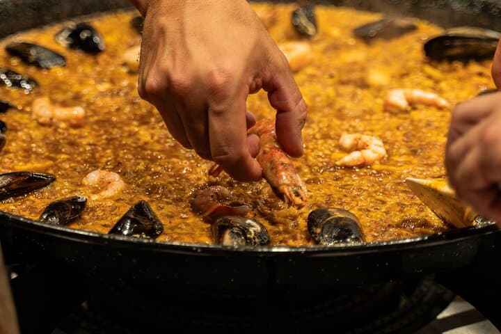 Get hands-on in the final stages of cooking! The participant is adding the prawns to our seafood paella - a key moment in creating the perfect, dish. The interactive, professional experience awaits!
