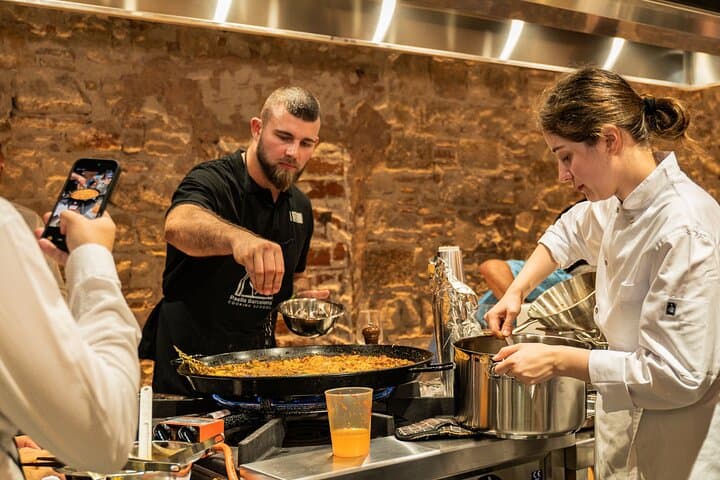 Master the technique! Chef Maria supervises as participants add premium seafood to the paella—an authentic moment worth filming in our hands-on cooking experience.
